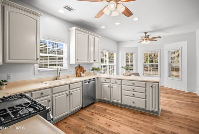 kitchen featuring light wood finished floors, visible vents, dishwasher, a peninsula, and a sink