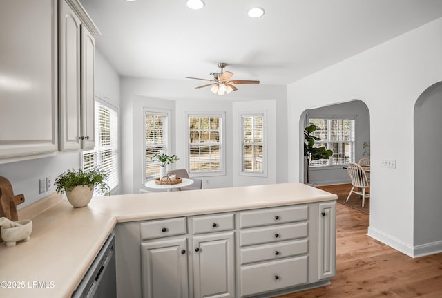 kitchen featuring baseboards, dishwasher, light wood-style flooring, a peninsula, and arched walkways