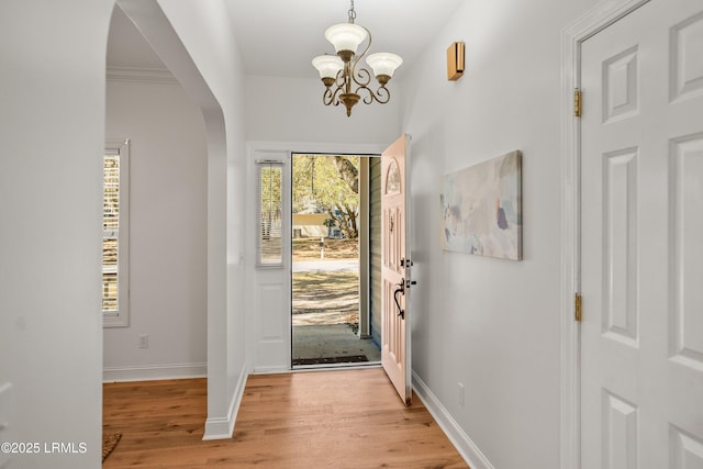 entrance foyer with arched walkways, light wood-style flooring, an inviting chandelier, and baseboards