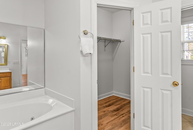 bathroom with baseboards, vanity, wood finished floors, and a whirlpool tub