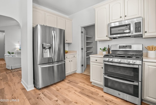 kitchen with arched walkways, light wood-style flooring, appliances with stainless steel finishes, and light countertops