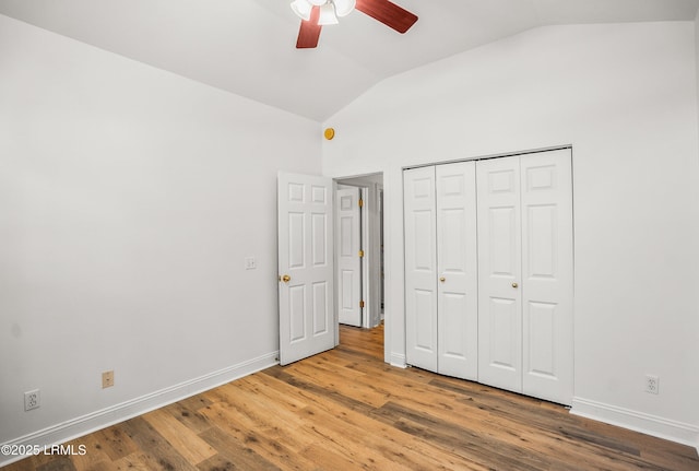 unfurnished bedroom with a closet, baseboards, wood finished floors, and vaulted ceiling