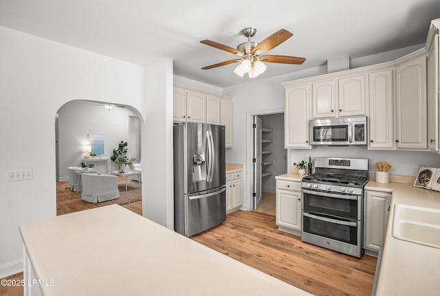 kitchen featuring light wood-style flooring, stainless steel appliances, arched walkways, light countertops, and ceiling fan