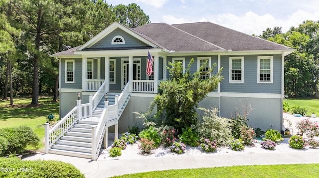 view of front of property with stucco siding, a porch, a front yard, a shingled roof, and stairs