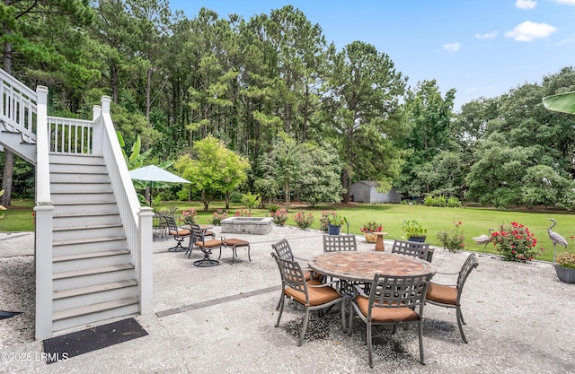 view of patio with an outbuilding, a shed, an outdoor fire pit, stairway, and outdoor dining area