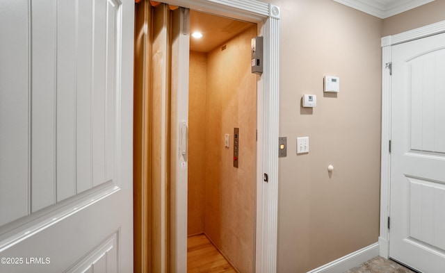 hall with baseboards, crown molding, elevator, and light wood-style floors