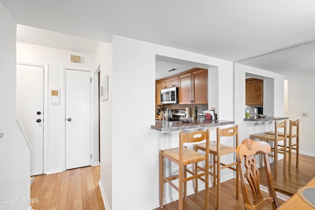 kitchen with stainless steel appliances, a breakfast bar area, brown cabinetry, light wood finished floors, and tasteful backsplash