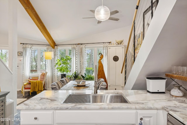 kitchen with a sink, vaulted ceiling with beams, light stone countertops, white cabinets, and stainless steel dishwasher