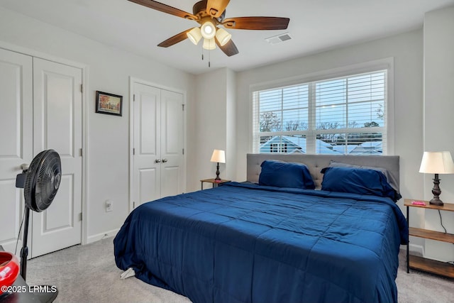 bedroom with two closets, light carpet, and ceiling fan