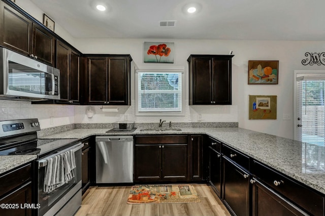 kitchen with sink, stainless steel appliances, light stone counters, dark brown cabinetry, and light wood-type flooring