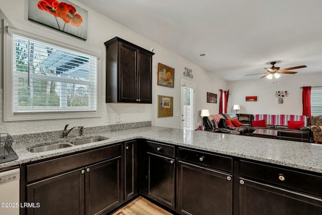 kitchen featuring white dishwasher, sink, light stone counters, and a healthy amount of sunlight