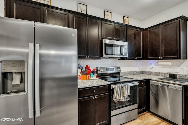 kitchen with stainless steel appliances, light wood-type flooring, dark brown cabinetry, and light stone counters