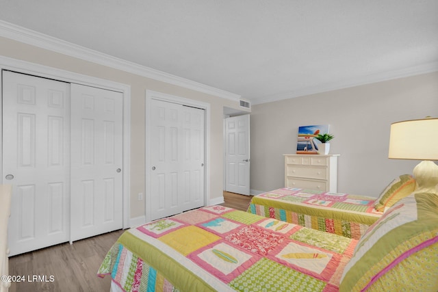 bedroom featuring multiple closets, ornamental molding, and light wood-type flooring