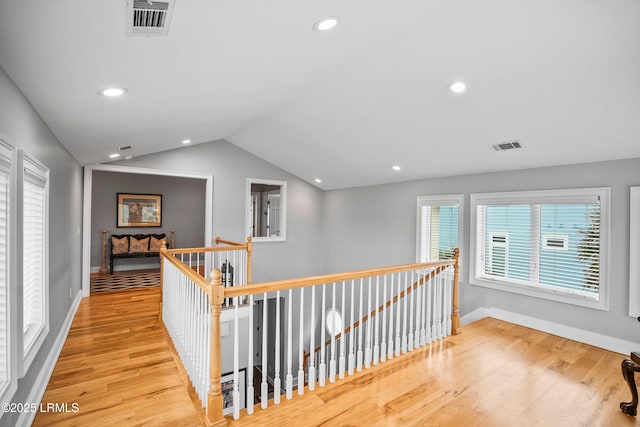 corridor with lofted ceiling, light wood finished floors, and an upstairs landing