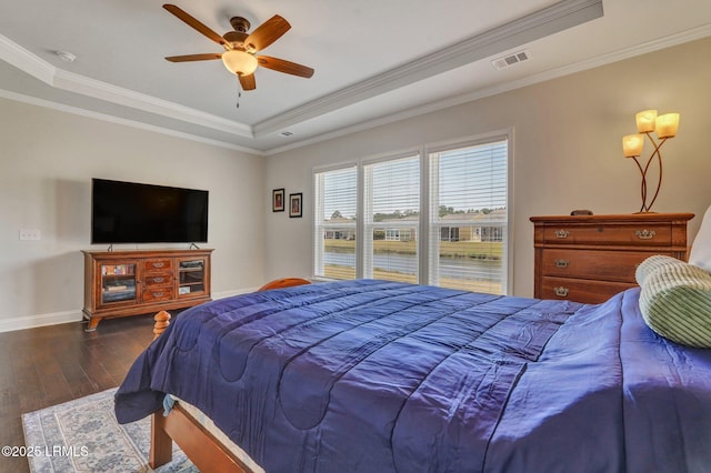 bedroom with visible vents, ornamental molding, a tray ceiling, wood finished floors, and baseboards