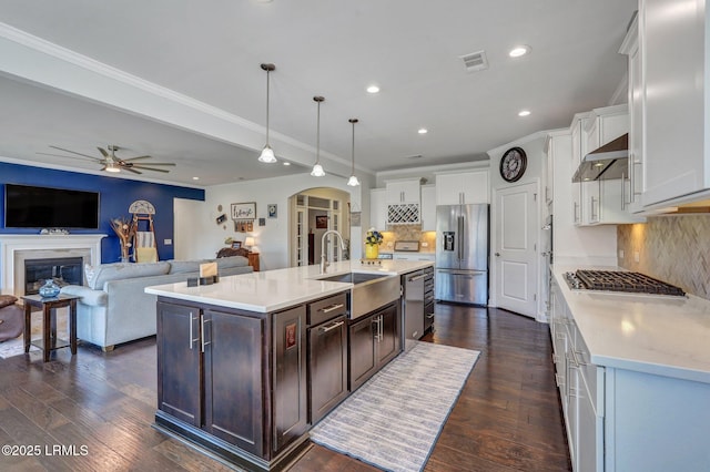 kitchen with ceiling fan, arched walkways, stainless steel appliances, wall chimney exhaust hood, and a sink