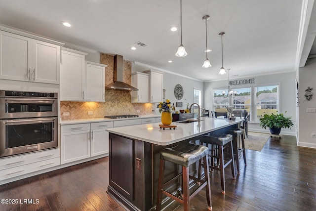 kitchen featuring gas stovetop, a sink, double oven, wall chimney range hood, and tasteful backsplash