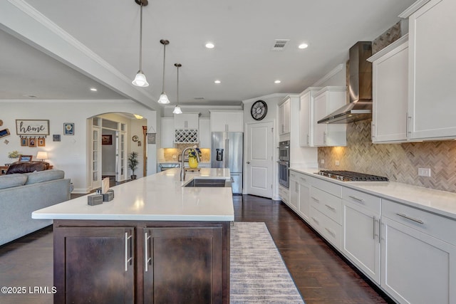 kitchen featuring visible vents, wall chimney range hood, appliances with stainless steel finishes, arched walkways, and a sink