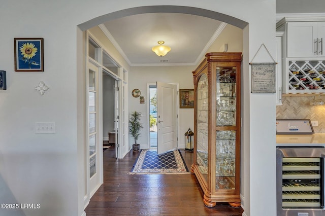 foyer featuring arched walkways, beverage cooler, and crown molding