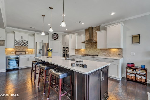 kitchen featuring dark wood-style flooring, stainless steel appliances, light countertops, wine cooler, and wall chimney range hood