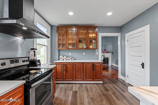 kitchen with stainless steel range with electric stovetop, wall chimney range hood, dark hardwood / wood-style flooring, and a brick fireplace