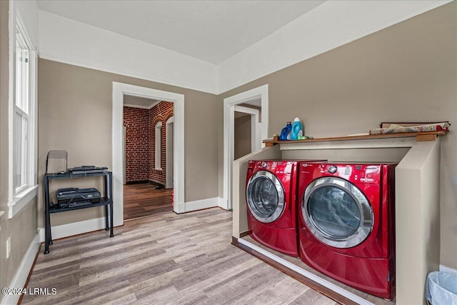 laundry area featuring independent washer and dryer, brick wall, and light wood-type flooring