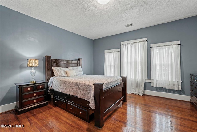 bedroom featuring multiple windows, dark hardwood / wood-style flooring, and a textured ceiling