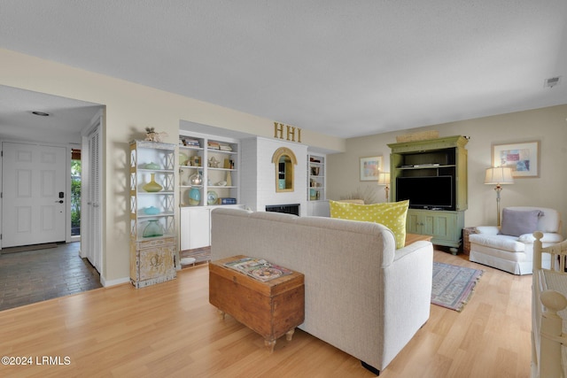 living room featuring hardwood / wood-style flooring, a fireplace, built in features, and a textured ceiling