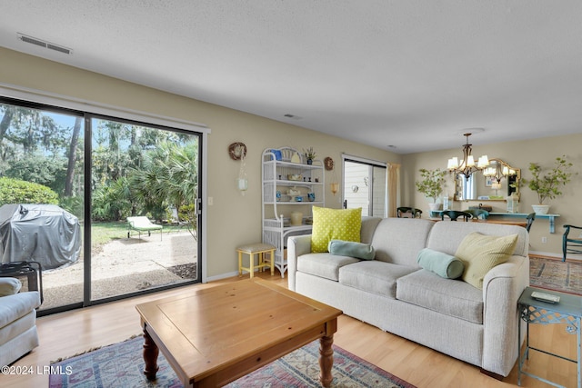 living room with a textured ceiling, a notable chandelier, and light wood-type flooring