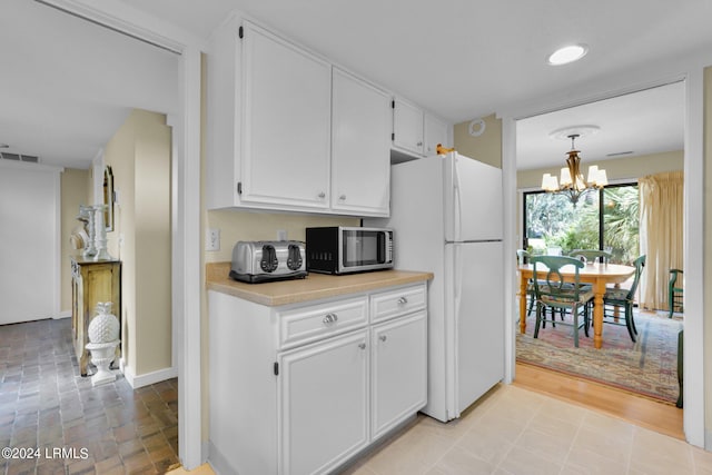 kitchen with white refrigerator, white cabinetry, a notable chandelier, and decorative light fixtures