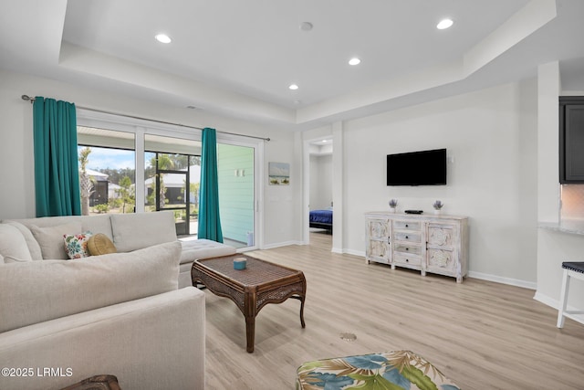 living area featuring baseboards, light wood-style flooring, recessed lighting, and a raised ceiling
