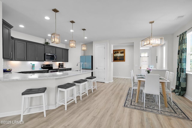 kitchen with a sink, backsplash, light wood finished floors, appliances with stainless steel finishes, and an inviting chandelier