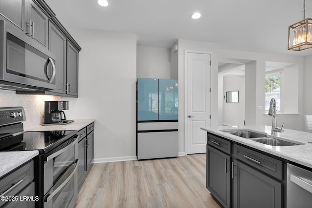 kitchen with gray cabinets, a sink, light wood-style flooring, stainless steel appliances, and decorative backsplash