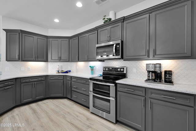 kitchen featuring backsplash, light stone countertops, stainless steel appliances, visible vents, and light wood-style floors