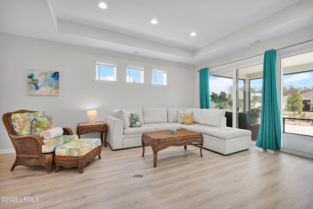 living room with baseboards, light wood-style flooring, recessed lighting, and a raised ceiling