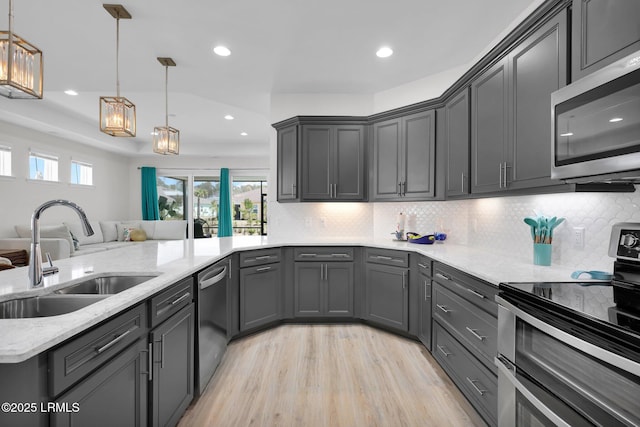 kitchen with stainless steel appliances, gray cabinetry, decorative backsplash, a sink, and light wood-style flooring