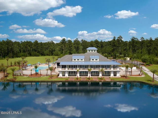 back of property featuring a water view, a balcony, an outdoor pool, and a wooded view