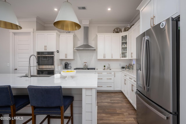 kitchen featuring wall chimney exhaust hood, stainless steel appliances, visible vents, and ornamental molding
