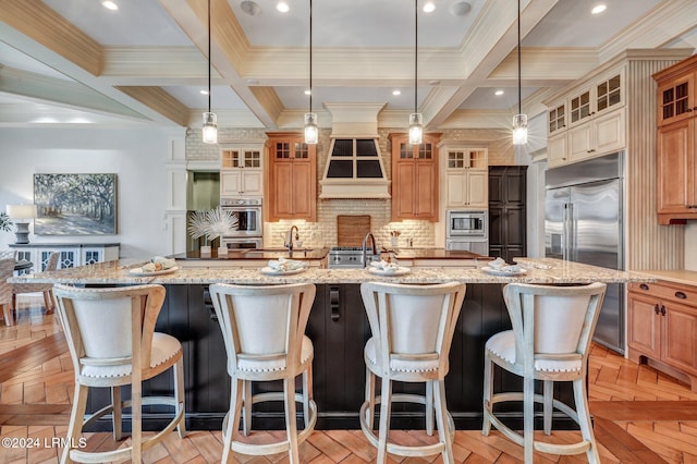 kitchen with tasteful backsplash, a large island with sink, light parquet floors, built in appliances, and light stone counters