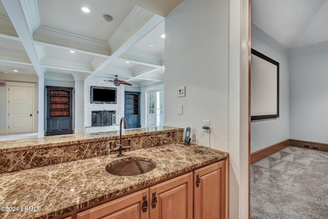 bathroom with coffered ceiling, a stone fireplace, crown molding, built in features, and beam ceiling