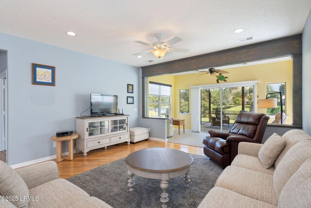 living room with ceiling fan, a textured ceiling, and light hardwood / wood-style flooring