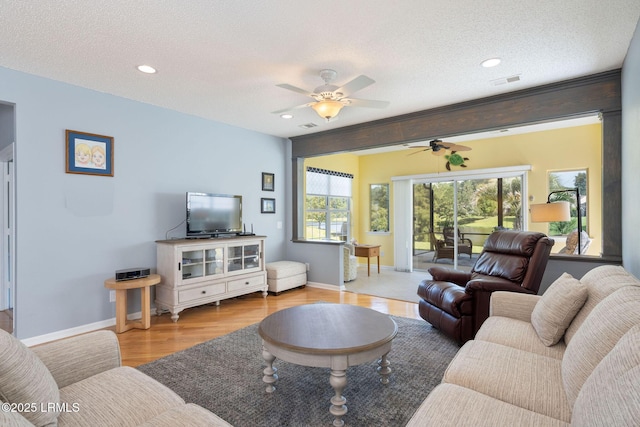 living room featuring light wood-type flooring, baseboards, a textured ceiling, and visible vents