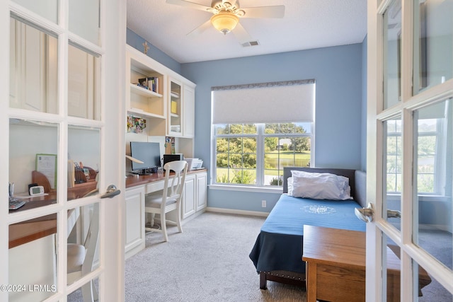 bedroom featuring ceiling fan, built in desk, and light colored carpet