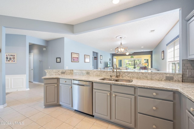 kitchen featuring light stone countertops, light tile patterned floors, gray cabinets, stainless steel dishwasher, and a sink