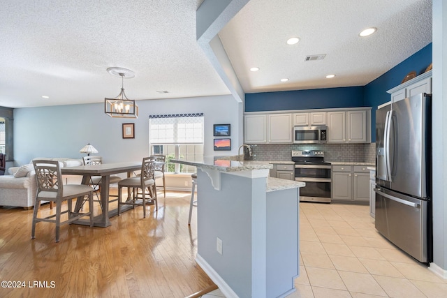 kitchen featuring visible vents, backsplash, light stone counters, appliances with stainless steel finishes, and a peninsula