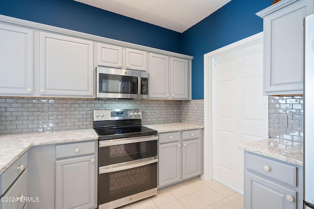 kitchen featuring light tile patterned floors, decorative backsplash, stainless steel appliances, and a textured ceiling