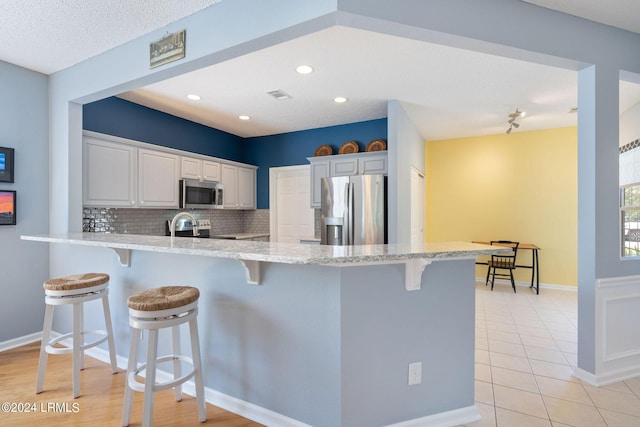 kitchen with a breakfast bar, white cabinetry, appliances with stainless steel finishes, kitchen peninsula, and backsplash