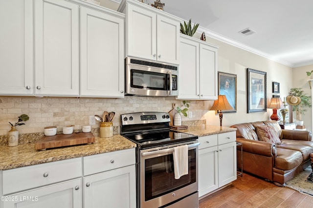 kitchen featuring light wood-style flooring, appliances with stainless steel finishes, open floor plan, ornamental molding, and backsplash