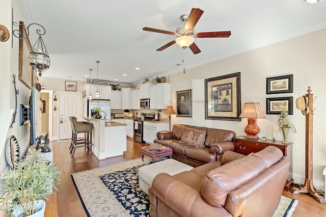 living area featuring ceiling fan, ornamental molding, light wood-style flooring, and baseboards