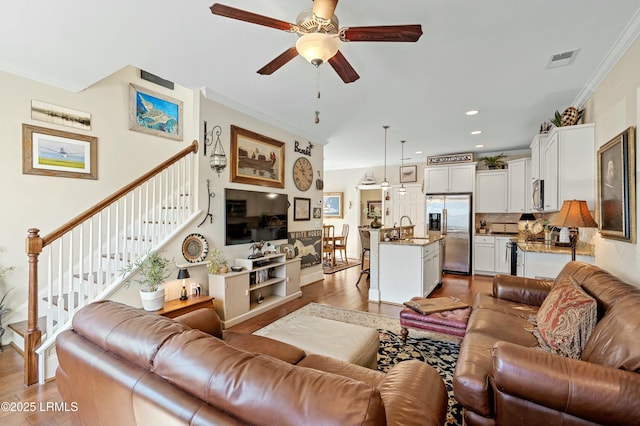 living area featuring light wood-style floors, stairs, visible vents, and ornamental molding